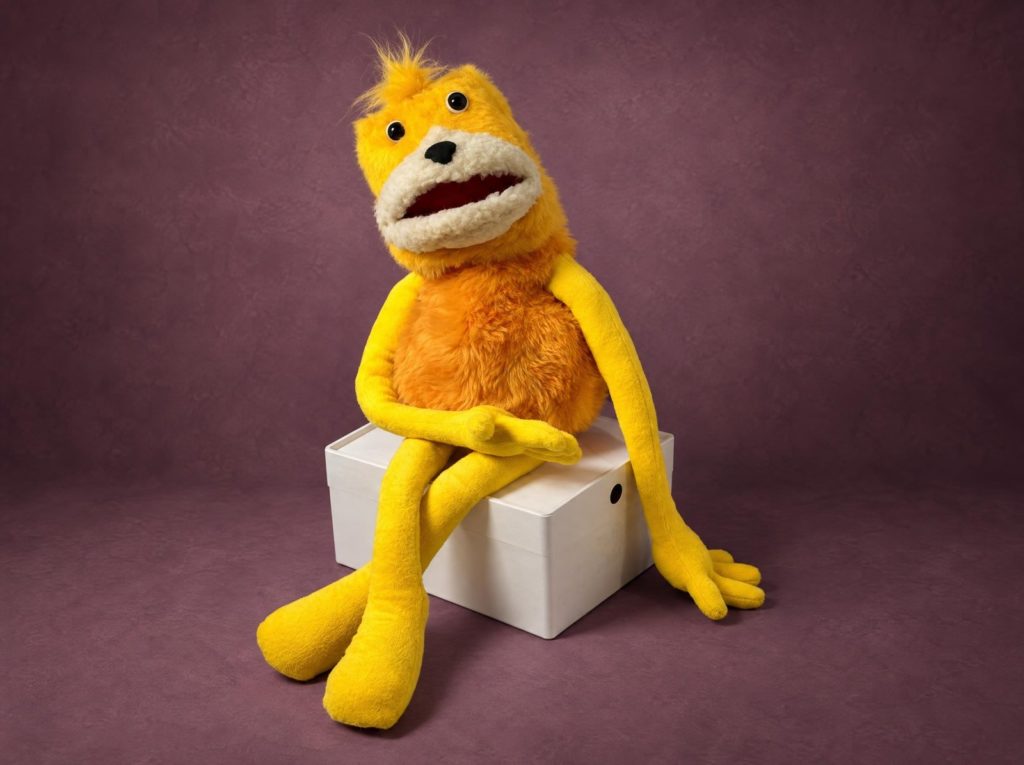 Flat Eric сложил длинные желтые руки на коленях, мягкая игрушка на заказ из искусственного меха