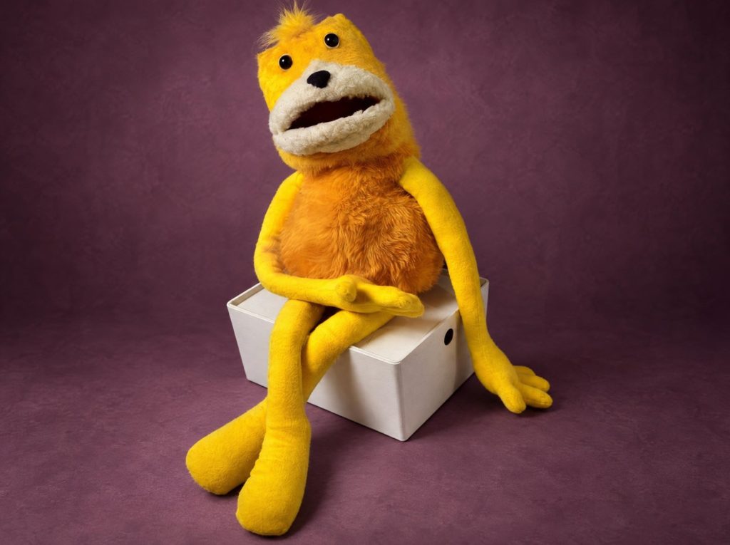 Flat Eric, мягкая игрушка на заказ: желтая голова, оранжевое тело и длинные руки на белой коробке
