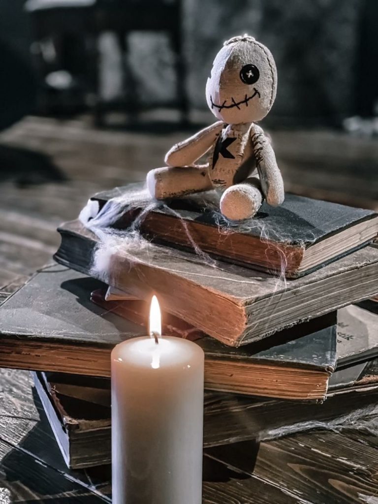 Кукла вуду на заказ сидит на старых книгах в паутине рядом с горящей свечой, кадр из фотосессии артиста